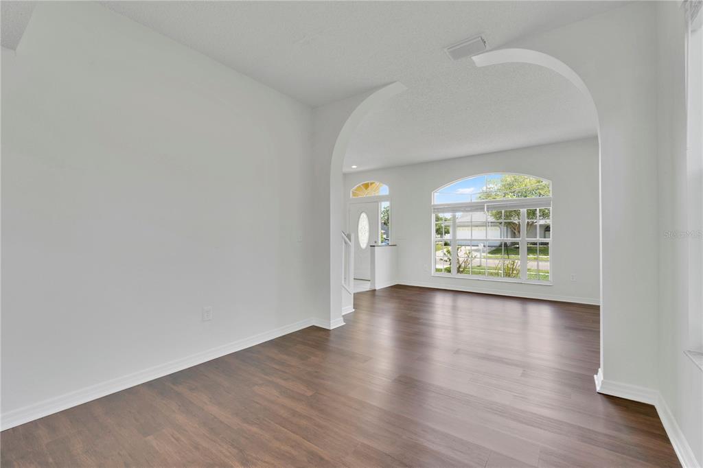 An empty room with dark wood flooring and a large arched entryway leading to an entrance — 1101 BLUFIELD AVENUE, BRANDON, FL