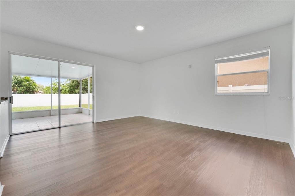 An empty room with wood-look flooring, white walls, a sliding glass door, and a window — 1101 BLUFIELD AVENUE, BRANDON, FL