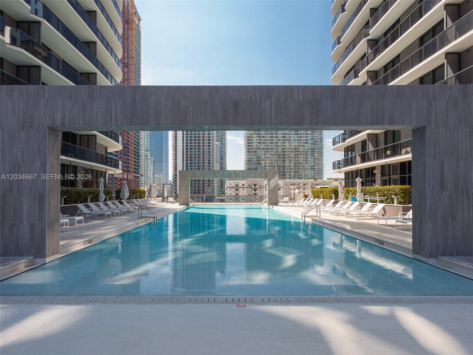A rectangular swimming pool is framed by a modern gray archway between two high-rise buildings — 55 SW 9 St # 1605, Miami FL 33130, MIAMI, FL