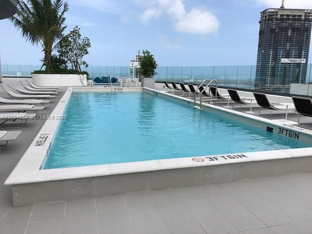 A rectangular rooftop swimming pool is surrounded by lounge chairs and a glass railing — 55 SW 9 St # 1605, Miami FL 33130, MIAMI, FL