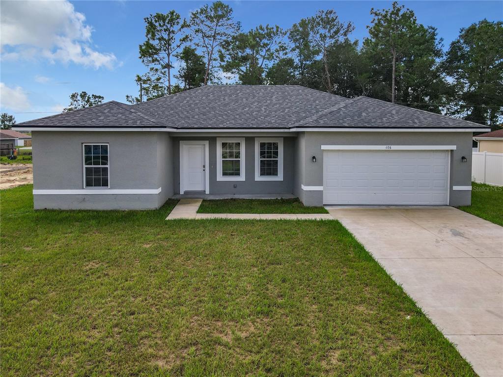 A single-story house with a gray stucco exterior, a white garage door, and a shingled roof — 406 MARION OAKS TRAIL, OCALA, FL