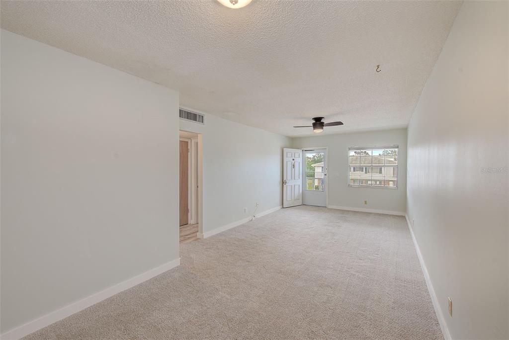 An empty living room features beige carpeting, light-colored walls, a ceiling fan, and a front door — 4742 AZALEA DRIVE UNIT 213, NEW PORT RICHEY, FL