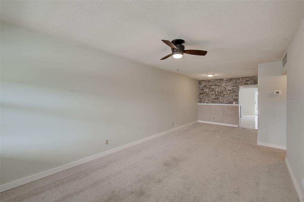 A carpeted living room features a ceiling fan, light gray walls, and a stone-accented wall — 4742 AZALEA DRIVE UNIT 213, NEW PORT RICHEY, FL