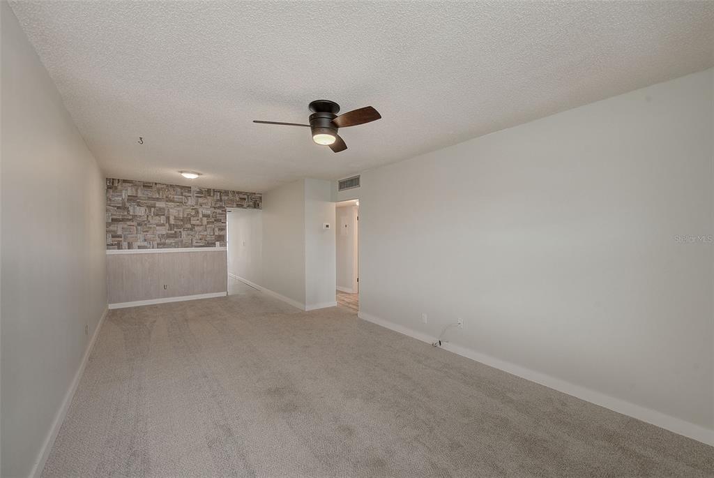 An empty living room features beige carpeting, a ceiling fan, and a stone-accented wall — 4742 AZALEA DRIVE UNIT 213, NEW PORT RICHEY, FL