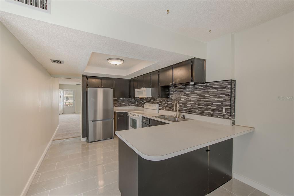 A kitchen with dark cabinets, stainless steel appliances, a tiled backsplash, and a breakfast bar — 4742 AZALEA DRIVE UNIT 213, NEW PORT RICHEY, FL