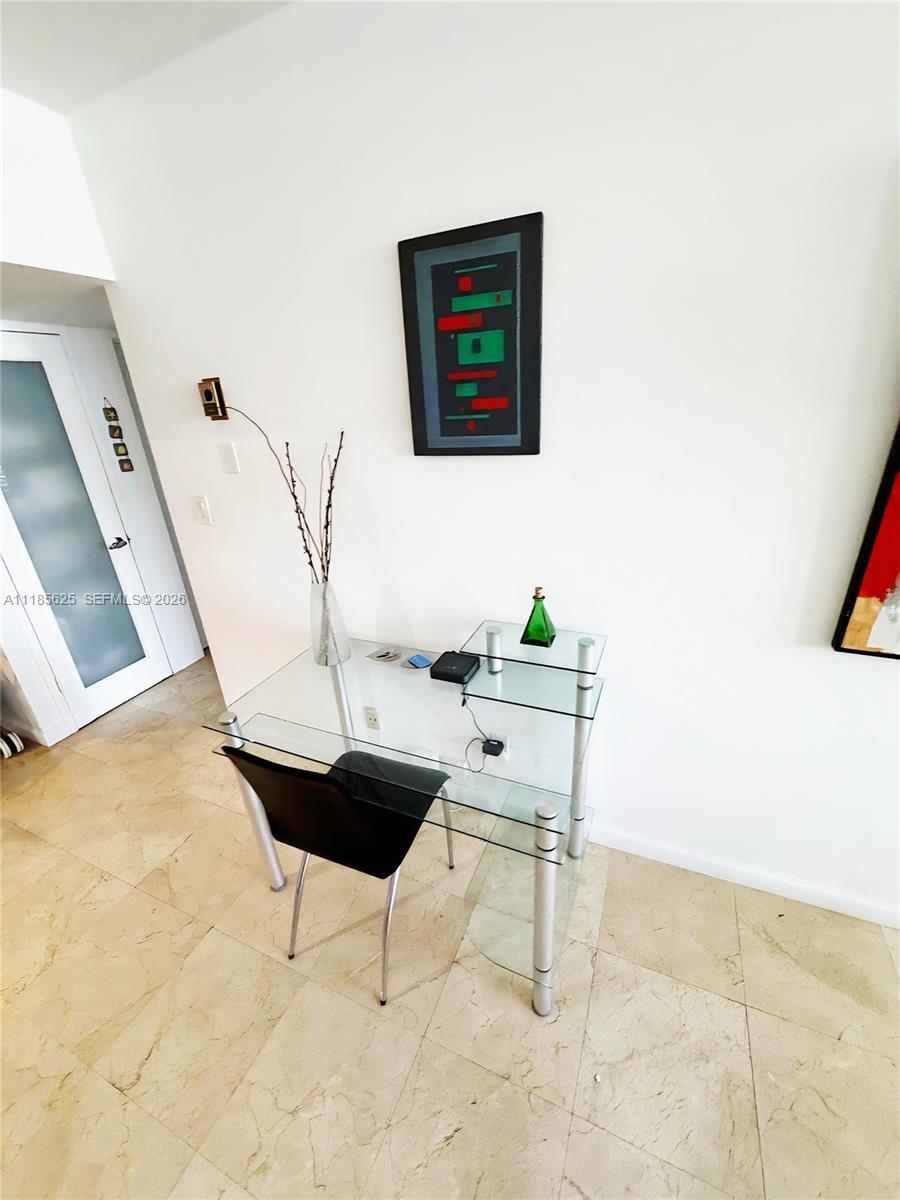 A glass desk with a black chair sits against a white wall with art — 100 Lincoln Rd # 1243, Miami Beach FL 33139, MIAMI BEACH, FL