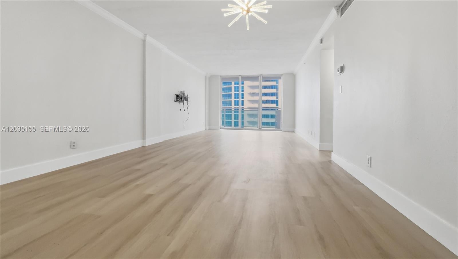 An empty living room features light wood-look flooring, white walls, and a balcony with windows — 3001 S Ocean Dr # 1415, Hollywood FL 33019, HOLLYWOOD, FL