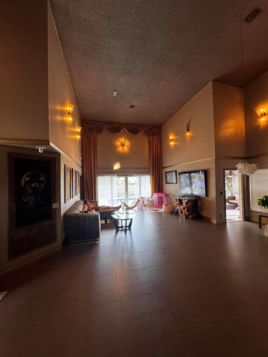A spacious living room with high ceilings, tile flooring, wall sconces, and a large window — 10302 Buena Ventura Drive, Boca Raton FL 33498, BOCA RATON, FL