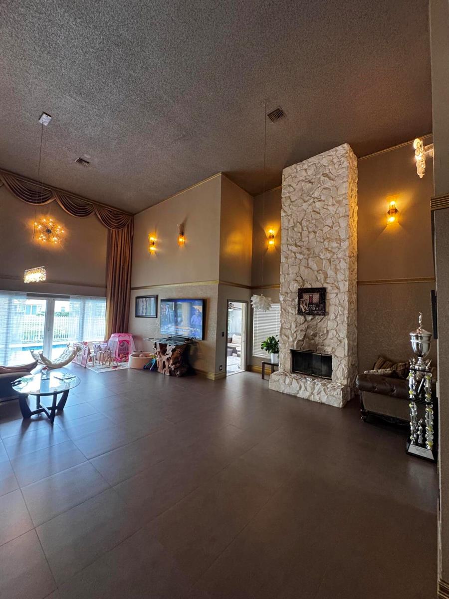 A spacious living room features high ceilings, a stone fireplace, and large windows with drapes — 10302 Buena Ventura Drive, Boca Raton FL 33498, BOCA RATON, FL