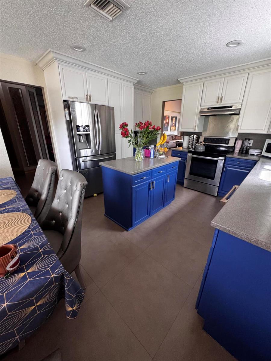 A kitchen features blue lower cabinets, white upper cabinets, a central island, and stainless appliances — 10302 Buena Ventura Drive, Boca Raton FL 33498, BOCA RATON, FL