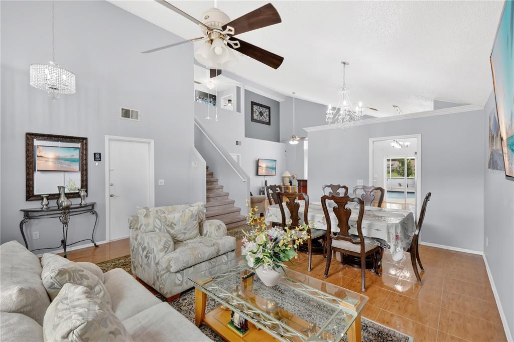 A living and dining area with high ceilings, tile floors, a staircase, and two chandeliers — 3047 STILLWATER DRIVE, KISSIMMEE, FL
