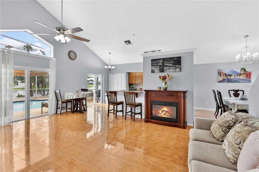 A bright open-concept living area features vaulted ceilings, tile flooring, a fireplace, and pool views — 3047 STILLWATER DRIVE, KISSIMMEE, FL