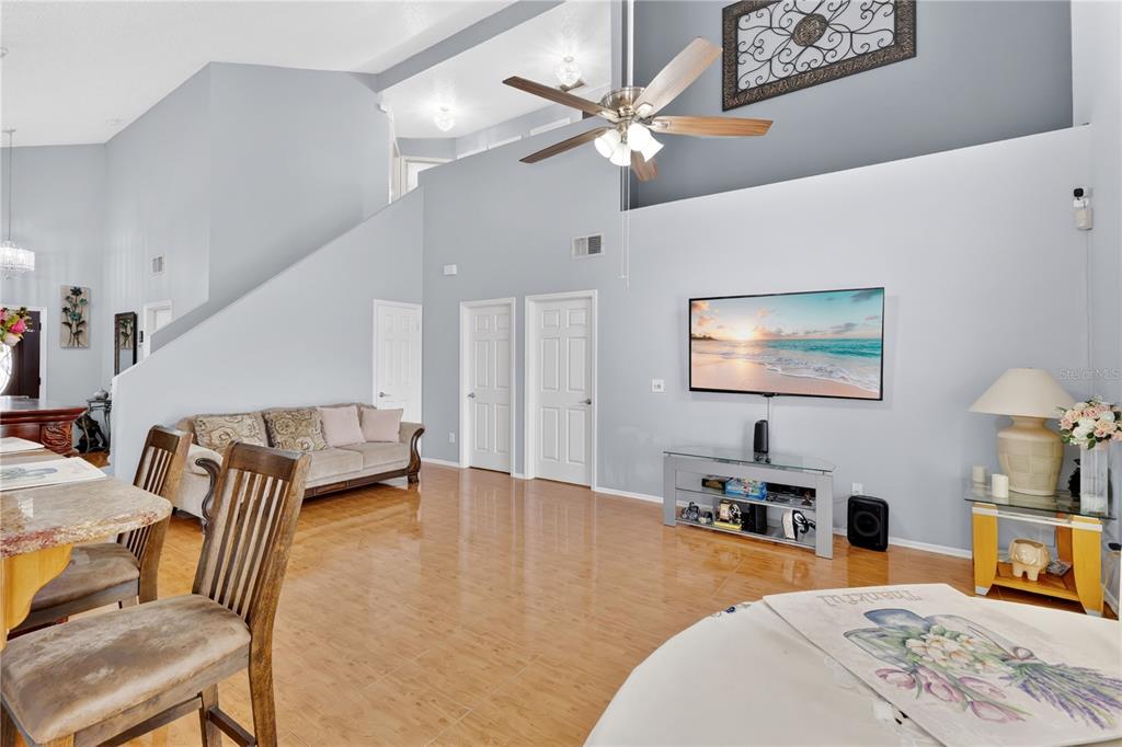 A living room with light blue walls, tile flooring, a ceiling fan, and a wall-mounted television — 3047 STILLWATER DRIVE, KISSIMMEE, FL