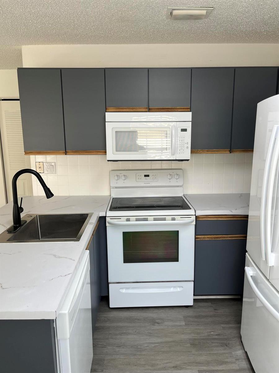 A kitchen features dark gray cabinets, white countertops, a white stove, and a stainless sink — 5665 Boynton Cove Way, Boynton Beach FL 33437, BOYNTON BEACH, FL