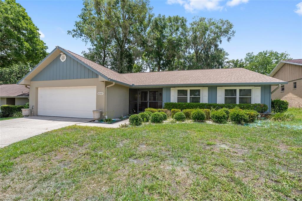 A single-story house with a two-car garage, tan siding, and a landscaped front yard — 8140 NW 48TH LANE, OCALA, FL