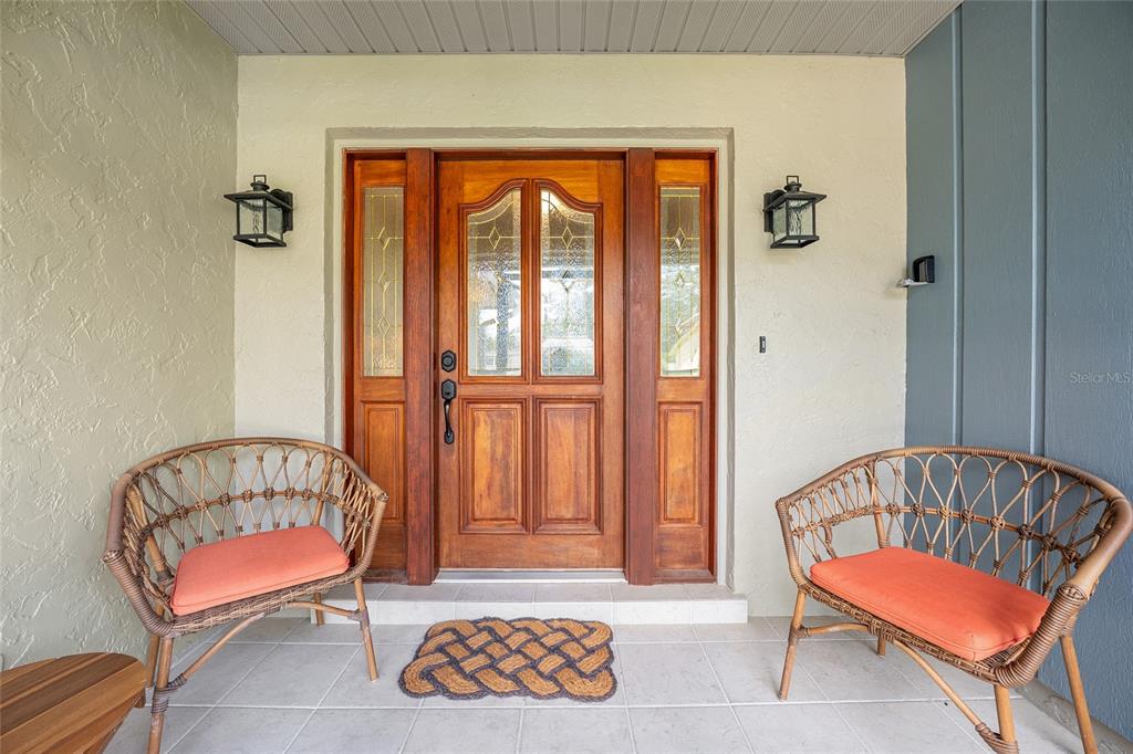 A covered entryway features a wooden front door with sidelights, two wicker chairs, and lanterns — 8140 NW 48TH LANE, OCALA, FL