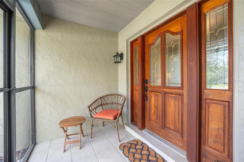 A covered porch features a wooden front door with glass panels, a chair, and table — 8140 NW 48TH LANE, OCALA, FL