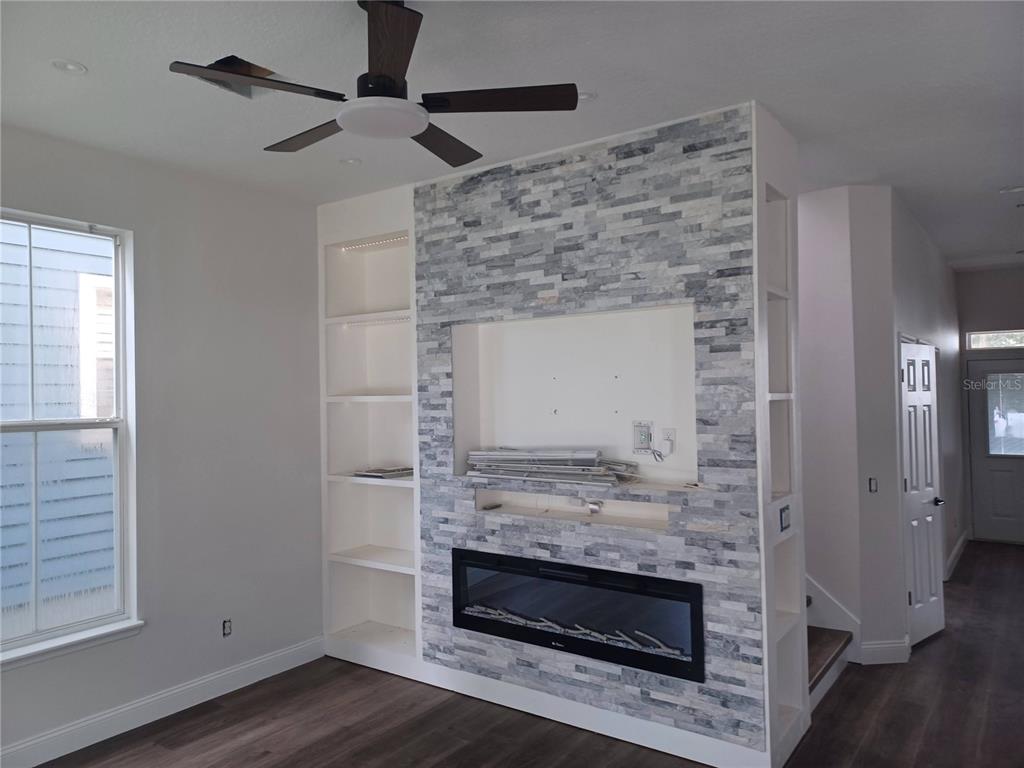 A living room features a stone-tiled fireplace wall with built-in shelving and a ceiling fan — 1010 PERIWINKLE COURT, CELEBRATION, FL