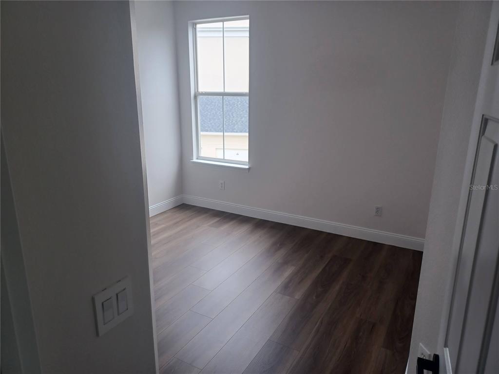 An empty room features wood-look flooring, white walls, and a single window — 1010 PERIWINKLE COURT, CELEBRATION, FL
