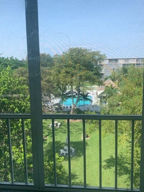 A view from a screened balcony overlooking a grassy courtyard, swimming pool, and apartment building — 4650 Washington St # 502, Hollywood FL 33021, HOLLYWOOD, FL