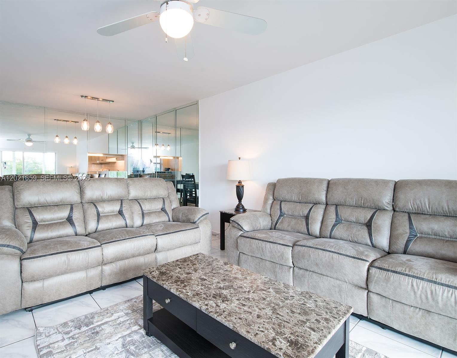 A living room features two gray reclining sofas, a marble-topped coffee table, and mirrored walls — 4650 Washington St # 502, Hollywood FL 33021, HOLLYWOOD, FL