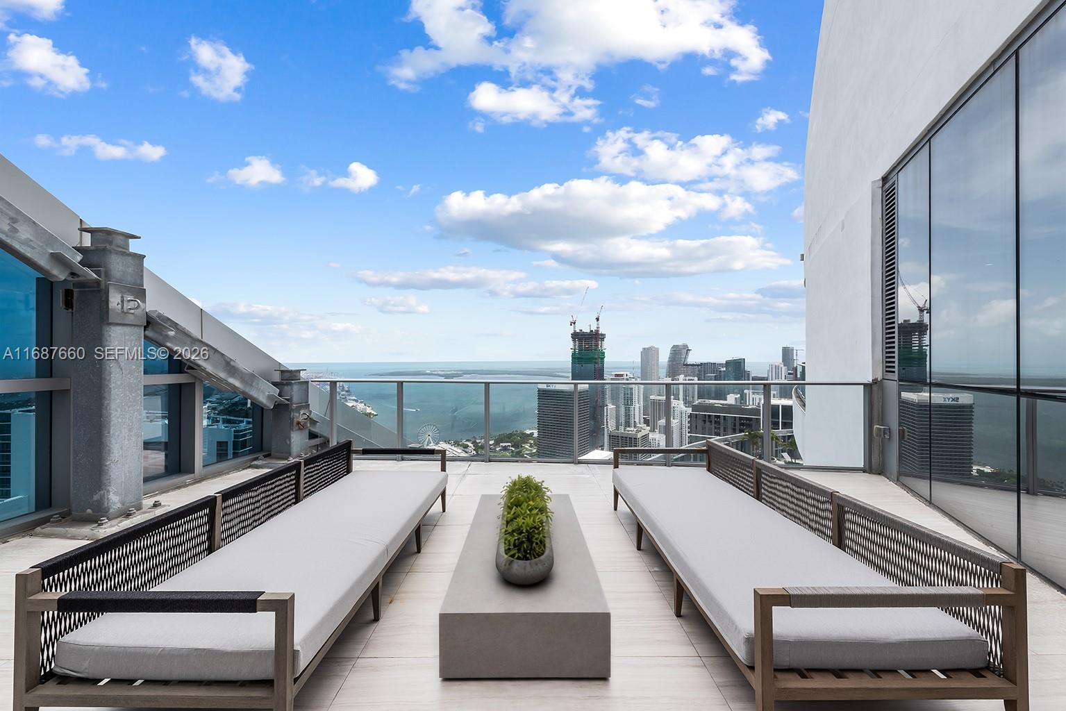 A high-rise balcony features two lounge chairs, a central planter, and a panoramic city view — 851 NE 1st Ave # 5700, Miami FL 33132, MIAMI, FL