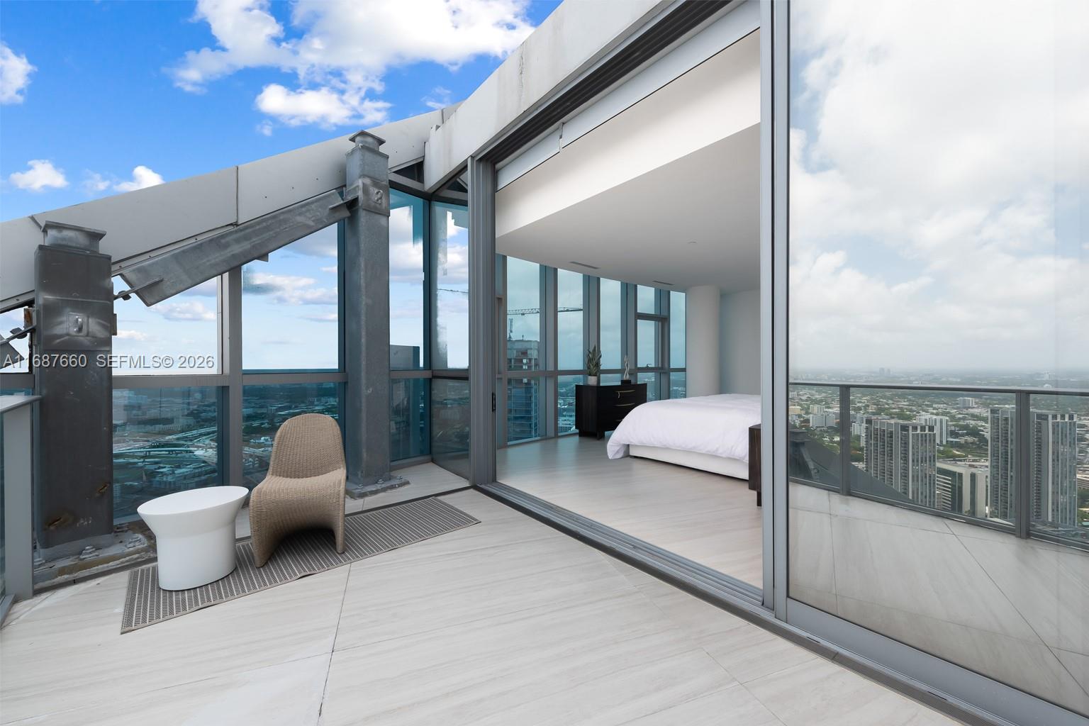 A bedroom with floor-to-ceiling windows opens onto a private balcony featuring a wicker chair — 851 NE 1st Ave # 5700, Miami FL 33132, MIAMI, FL