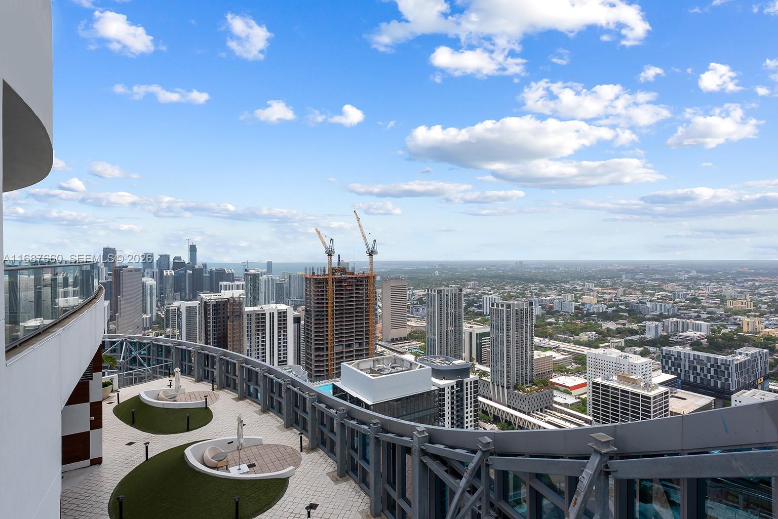 A high-rise balcony overlooks a dense urban cityscape with several skyscrapers and construction cranes — 851 NE 1st Ave # 5700, Miami FL 33132, MIAMI, FL