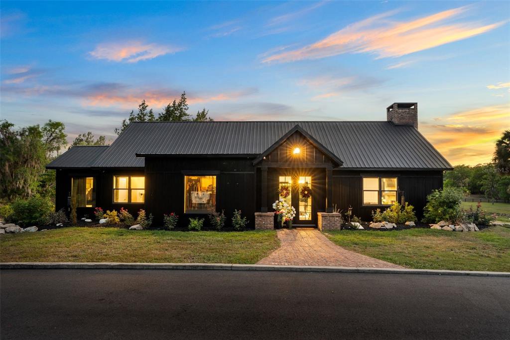 A black farmhouse-style home with a metal roof and brick walkway at sunset — 17995 NE 24TH TERRACE, CITRA, FL