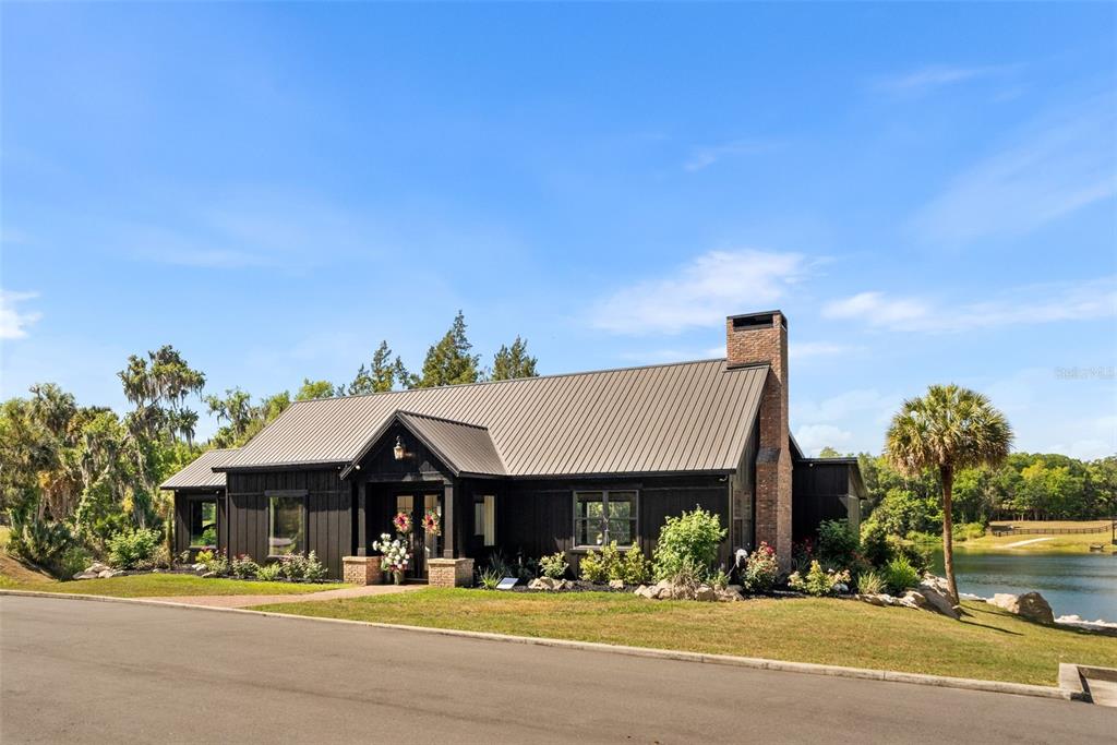 A black house with a metal roof and brick chimney sits beside a lake — 17995 NE 24TH TERRACE, CITRA, FL