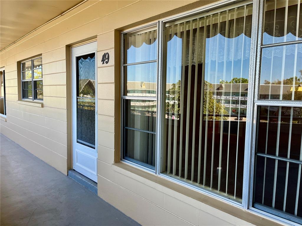 A tan exterior wall features a white door labeled 49 and large windows with blinds — 2041 AUSTRALIA WAY W UNIT 49, CLEARWATER, FL