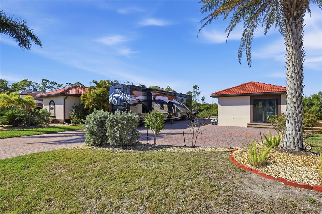 A large RV is parked on a paved driveway between two small, tile-roofed buildings — 14100 MYAKKA AVENUE UNIT 26, PORT CHARLOTTE, FL