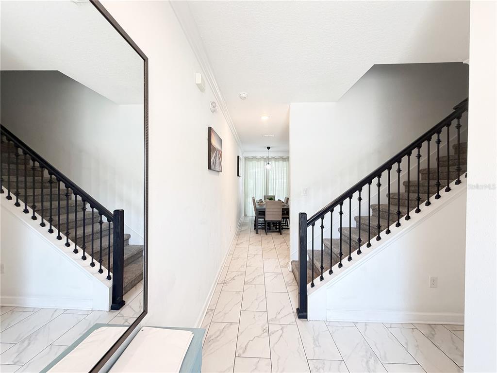 A hallway with white tile floors leads to a dining area between two carpeted staircases — 4192 PARAGRAPH DRIVE, KISSIMMEE, FL