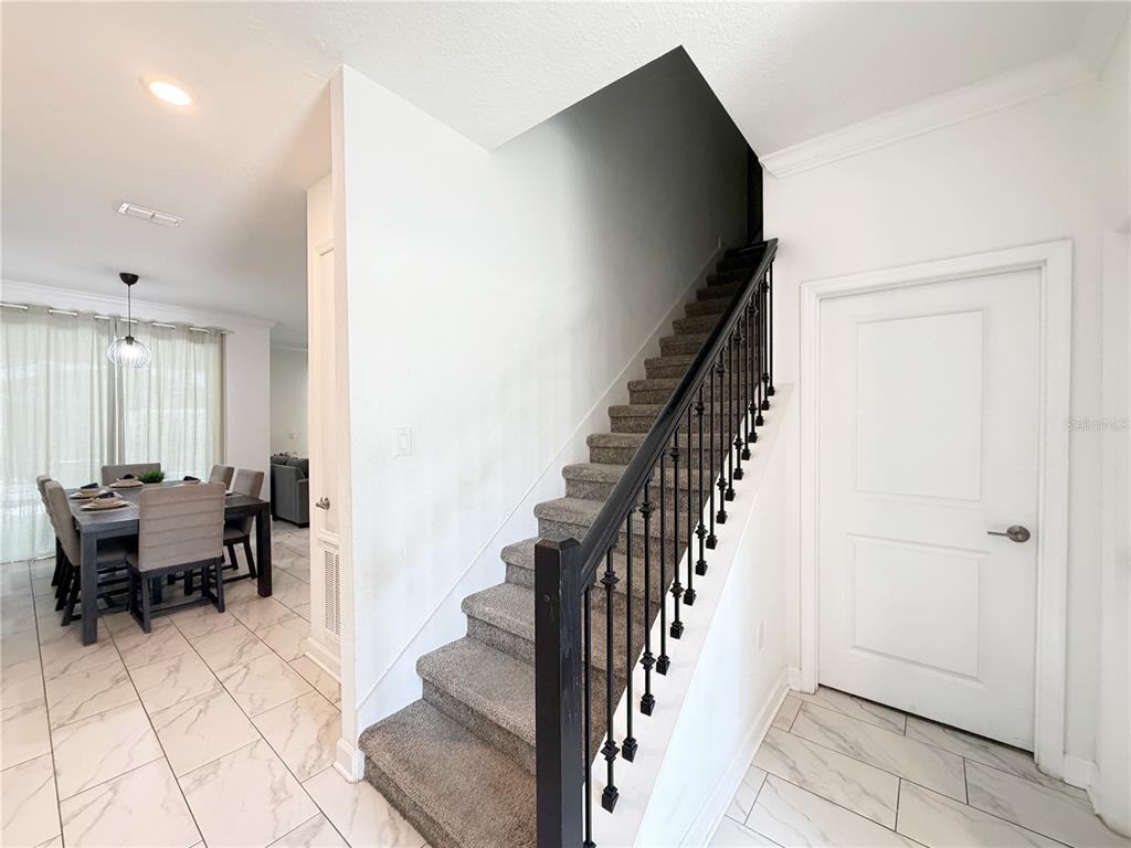 A carpeted staircase with a black metal railing sits next to a dining area — 4192 PARAGRAPH DRIVE, KISSIMMEE, FL