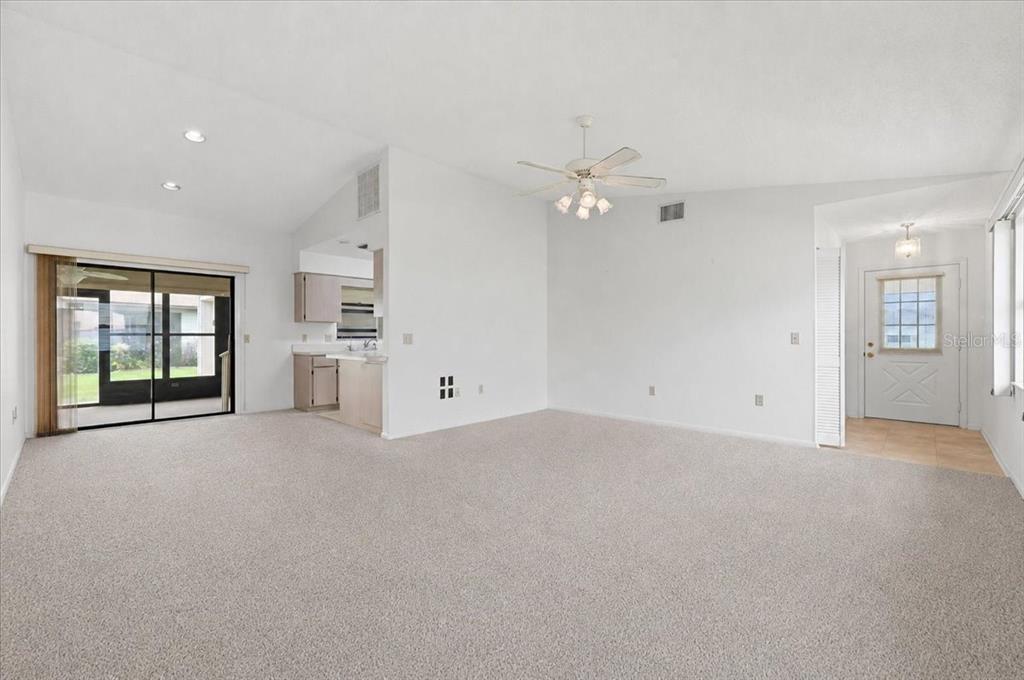 A spacious living room features beige carpeting, white walls, a ceiling fan, and sliding glass doors — 3741 INNISBROOK DRIVE, LAKELAND, FL