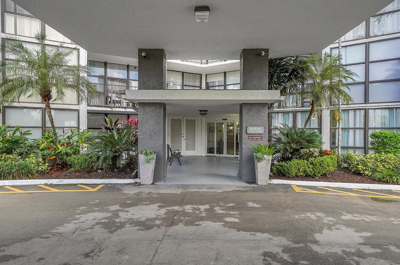 The exterior entrance of a multi-story building features a covered driveway and tropical landscaping — 1000 Parkview Drive # 306, Hallandale Beach FL 33009, HALLANDALE BEACH, FL