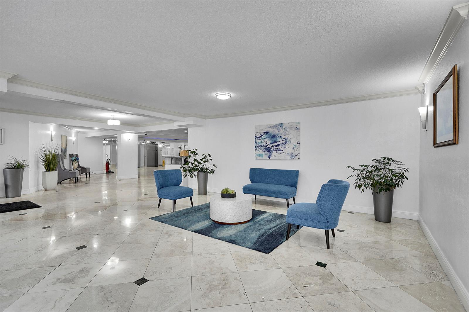 A bright lobby features blue seating, a round coffee table, and marble tile flooring — 1000 Parkview Drive # 306, Hallandale Beach FL 33009, HALLANDALE BEACH, FL