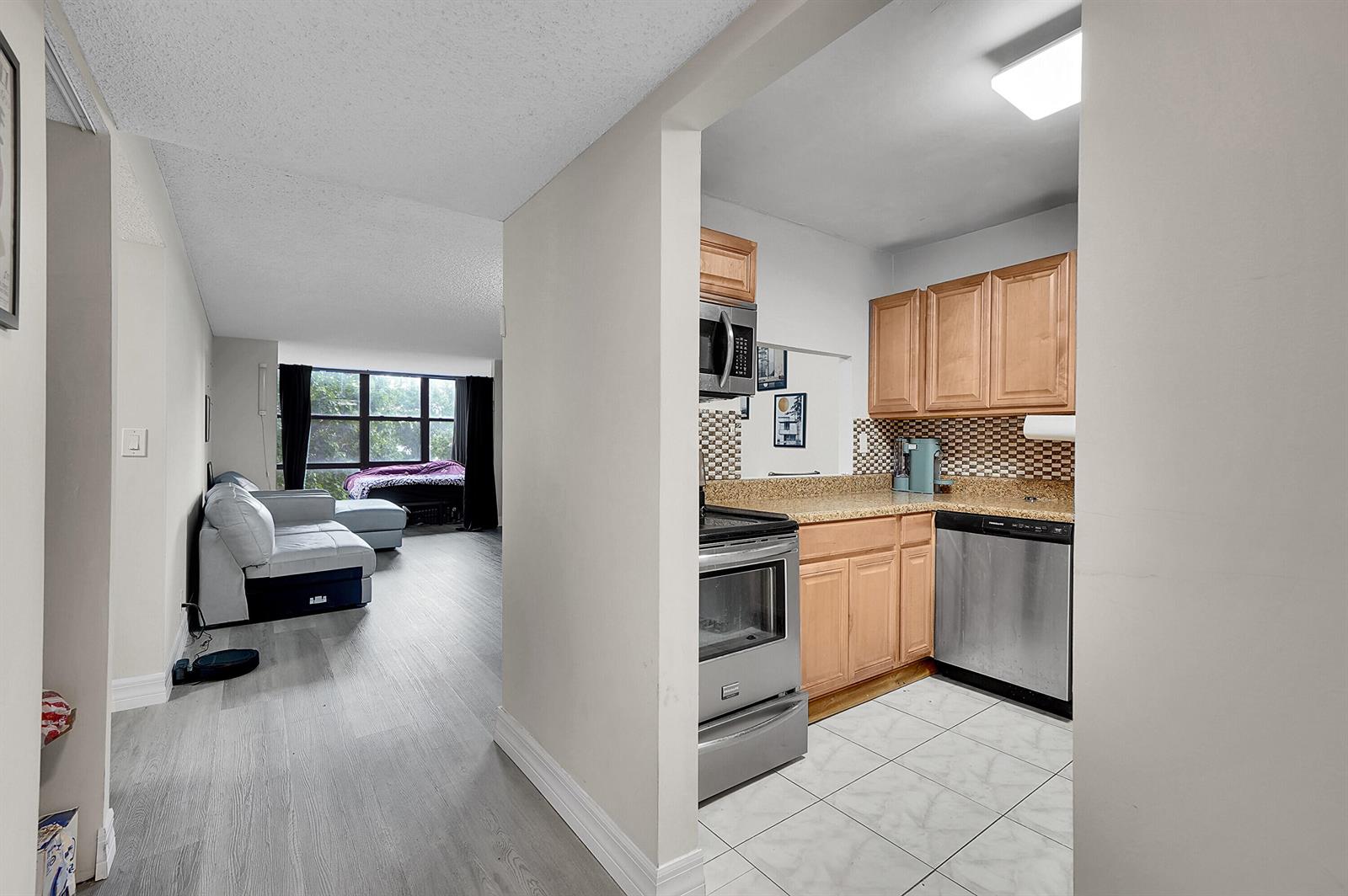 A view from a hallway into a kitchen with light wood cabinets and a living area — 1000 Parkview Drive # 306, Hallandale Beach FL 33009, HALLANDALE BEACH, FL