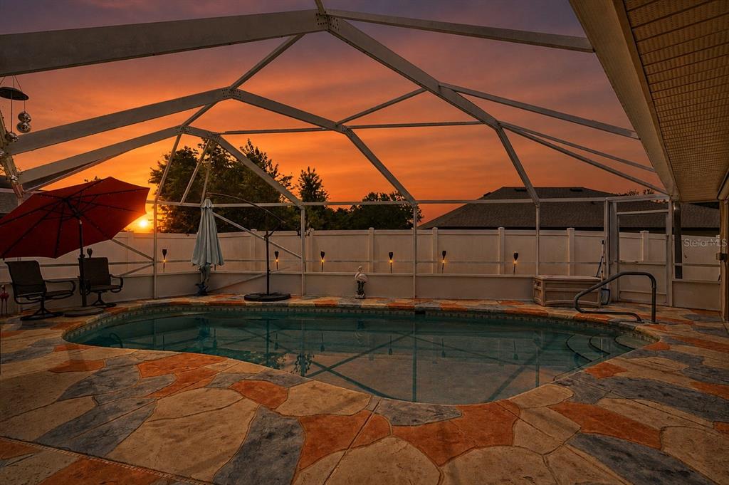 A swimming pool with a screened enclosure and decorative stone patio at sunset — 33939 VALENCIA DRIVE, LEESBURG, FL