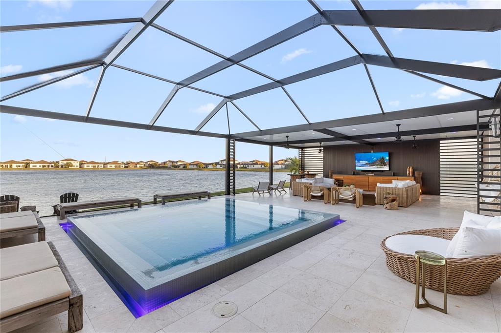 A screened-in patio features a raised infinity pool overlooking a lake with outdoor seating — 4796 SOPHIA DRIVE, AVE MARIA, FL
