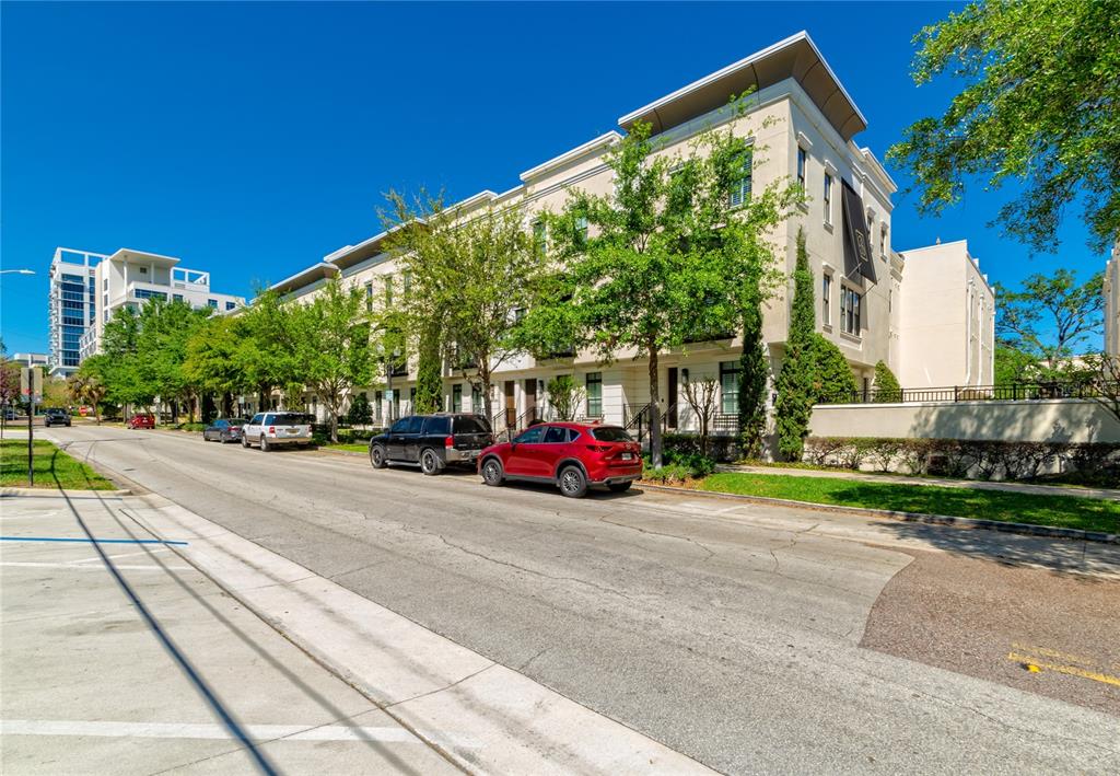 A street-level view of a multi-story, light-colored townhouse complex with parked cars — 653 E JACKSON STREET, ORLANDO, FL