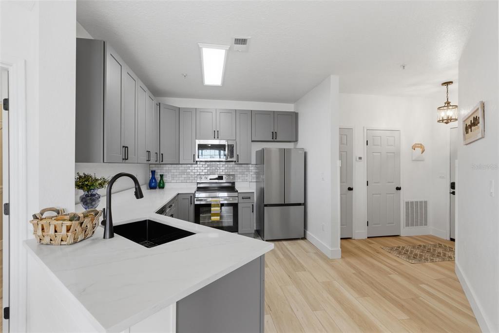 A kitchen features gray cabinets, stainless steel appliances, a black sink, and light wood flooring — 4323 BAYSIDE VILLAGE DRIVE UNIT 312, TAMPA, FL