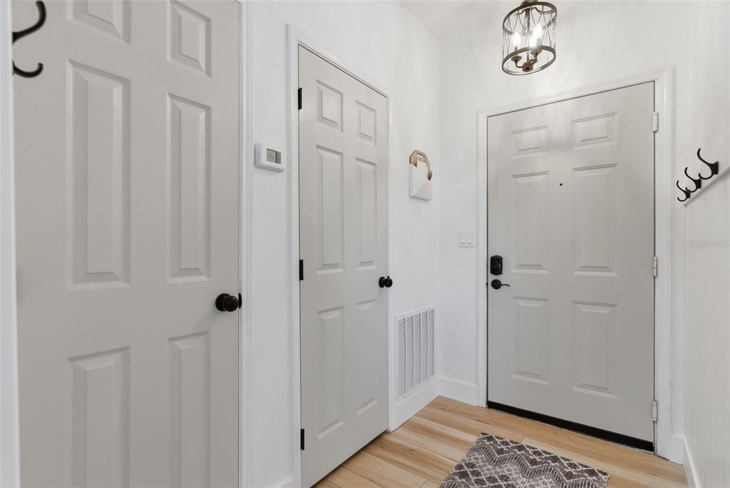 An entryway features white walls, light wood flooring, three doors with black hardware, and a light — 4323 BAYSIDE VILLAGE DRIVE UNIT 312, TAMPA, FL