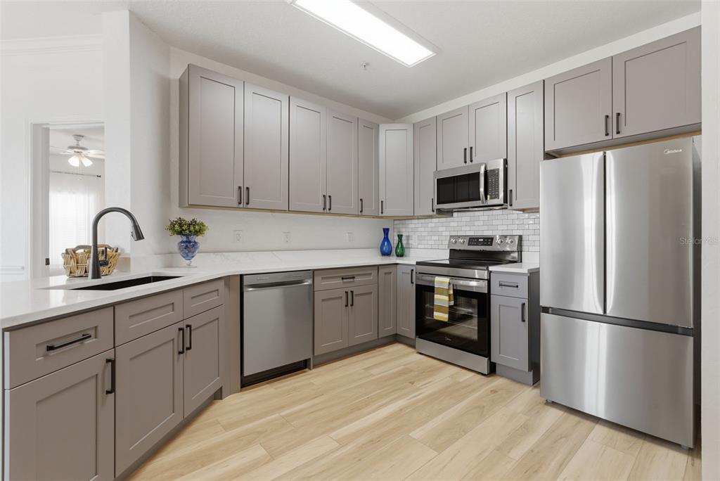A modern kitchen features gray cabinets, stainless steel appliances, white countertops, and light wood flooring — 4323 BAYSIDE VILLAGE DRIVE UNIT 312, TAMPA, FL