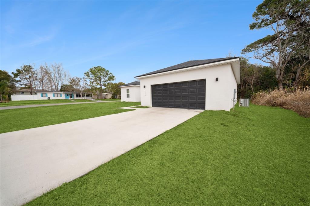 A white house exterior with a dark garage door and a concrete driveway — 1523 ZINNIA DRIVE, DELTONA, FL