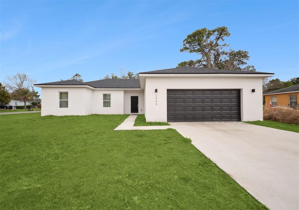 A single-story white house with a dark garage door and a concrete driveway — 1523 ZINNIA DRIVE, DELTONA, FL