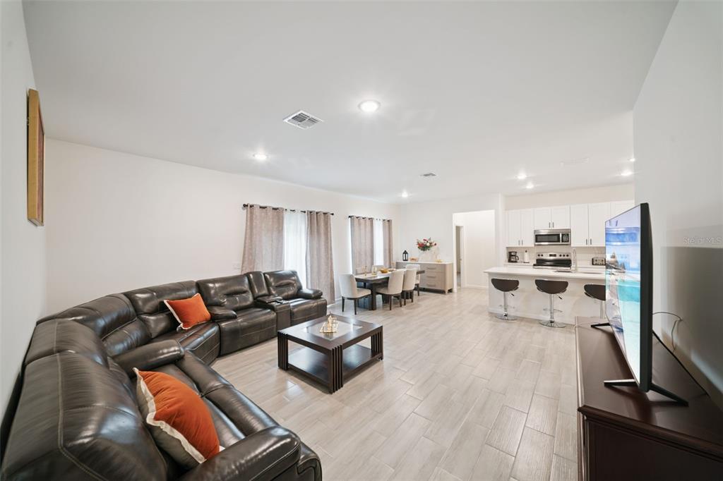 A spacious open-concept living room features a dark leather sectional, dining area, and modern kitchen — 1523 ZINNIA DRIVE, DELTONA, FL