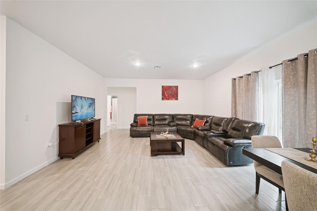 A living room features light wood-look tile flooring, a dark leather sectional, and a television console — 1523 ZINNIA DRIVE, DELTONA, FL