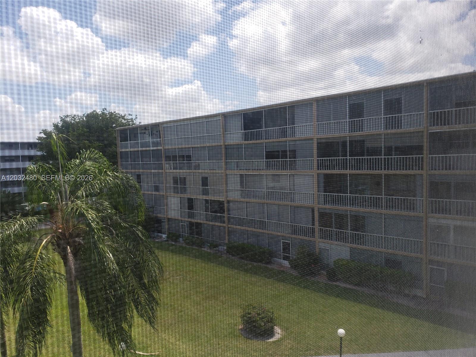 A view from a window shows a multi-story apartment building overlooking a grassy lawn — 4700 Washington St # 404, Hollywood FL 33021, HOLLYWOOD, FL