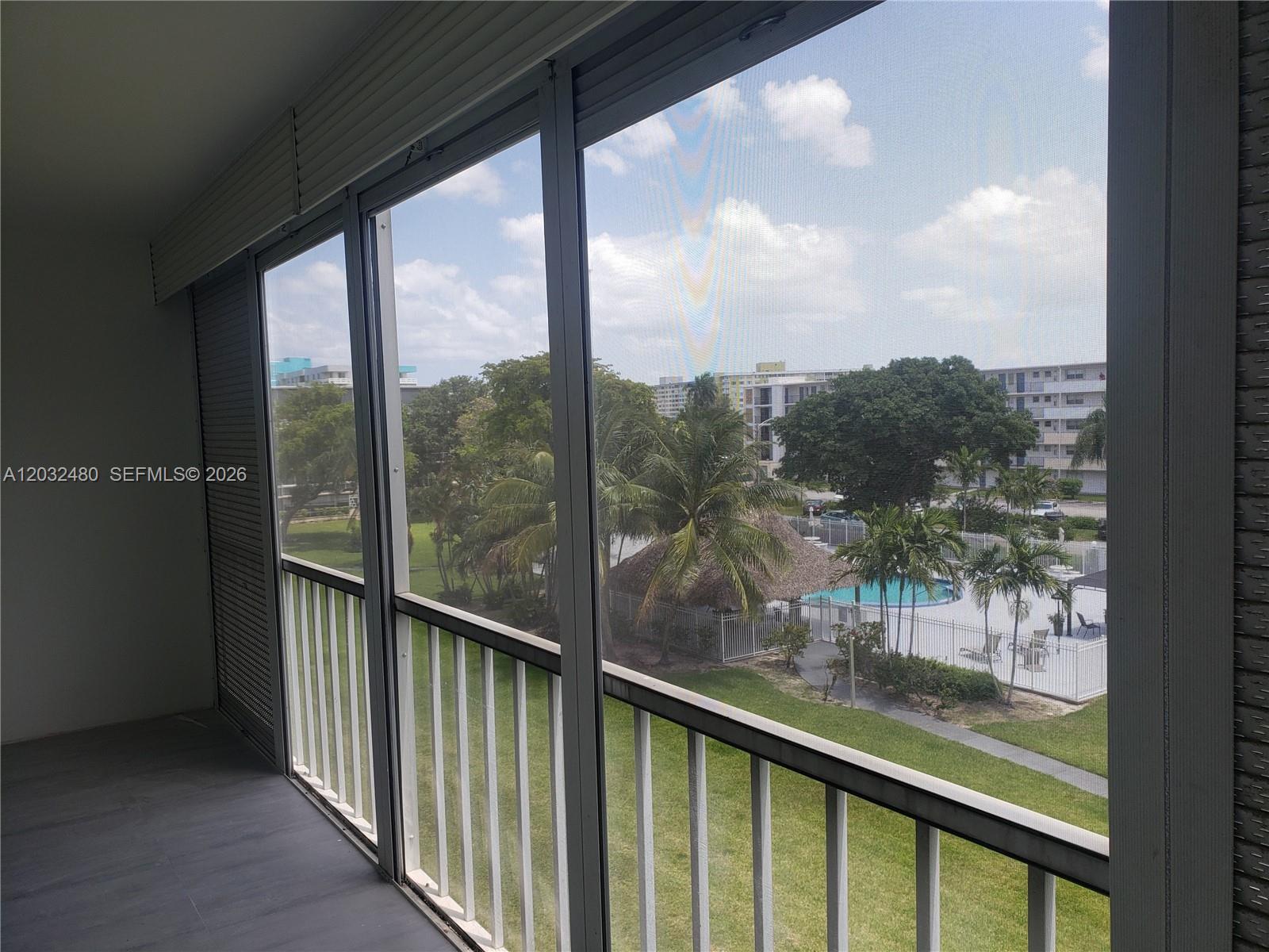 A screened-in balcony overlooks a swimming pool, palm trees, and apartment buildings — 4700 Washington St # 404, Hollywood FL 33021, HOLLYWOOD, FL
